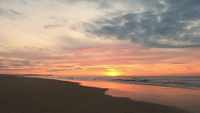 This serene slow-motion footage showcases the magnificent display of colors as the sun sets over a tranquil beach. The peaceful atmosphere is heightened by the gentle motion of the waves, the soft