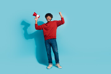Full body portrait of delighted cheerful guy raise fist hold loudspeaker achievement empty space isolated on blue color background