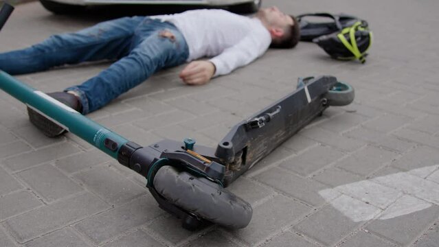Aftermath of accident car collided with electric scooter leaving scooter driver injured on ground. Injured individual now primary victim of collision requires immediate medical attention.