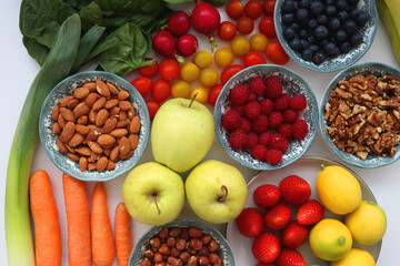 Apples, lemons, bananas, berries, carrots, leek, tomatoes, radishes, spinach and various nuts on white background. Healthy seasonal fruit and vegetable. Top view.