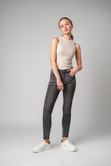 Girl in Beige Tank Top and Grey Jeans on gray background