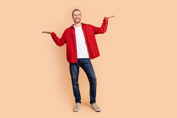 Full length portrait of nice young man arms show empty space ad wear red shirt isolated on beige color background