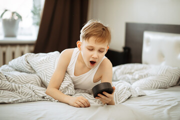 Kid boy teenager waking up yawning and stopping alarm clock in morning