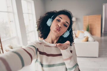 Photo of flirty cute lady dressed striped pullover earphones sending you kiss recording video indoors apartment room - obrazy, fototapety, plakaty