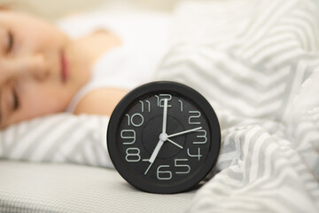 Alarm clock on bed. Cute kid girl sleeping on the background.