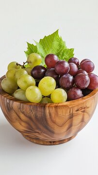 Delicious green and red grapes with leaves in a wooden bowl, isolated on white background