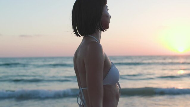 Summer mood. Sensual woman in white bikini, swimwear posing on the beach. beautiful young woman enjoying her holiday on the seashore. Sexy tanned girl. Sunset light. A woman enjoys the sunset.
