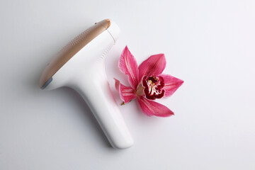 Magenta flower petal next to hair removal device on white surface