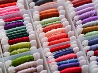 A lot of plastic bobbins with different colour embroidery threads in a plastic sorting box.