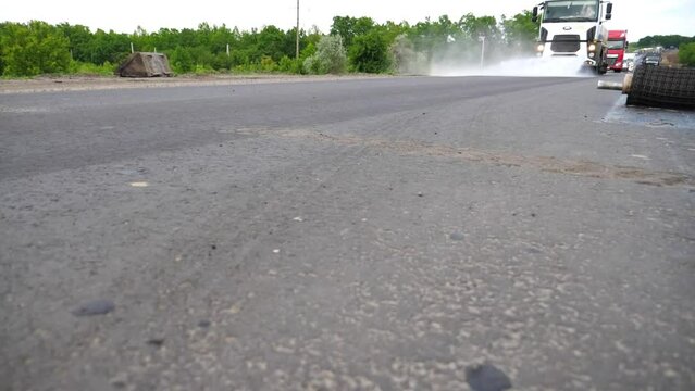Big vehicle washing new asphalt road with water splashing. Car with washing tank spraying water to road after roadwork. Concept of constructing highway. Roadway repair