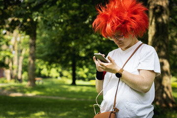 Portrait of a caucasian woman in a red wig with a phone in the park.