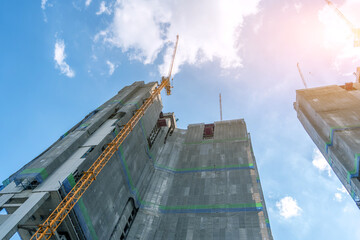 High rise towers in the scaffolding are covered with technical fabric with a protective tarpaulin with cranes on top, against the background bright sun
