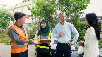 Man in light blue shirt talks to a veiled woman and one in white blazer, outdoor, car hood open....