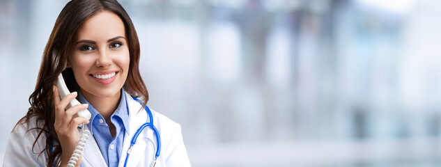 Portrait of happy smiling female doctor on phone, against blurred modern office background. Medical call center concept picture. Wide banner composition image with empty ad slogan text area.
