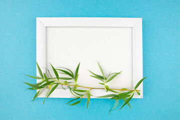 wooden photo frame and branch with leaves on isolated blue background