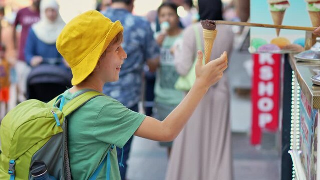 A playful moment unfolds as a boy anticipates the taste of creamy Turkish ice cream, only to be met with the mischievous antics of a skilled vendor. Amid the vibrant market bustle, the vendor's