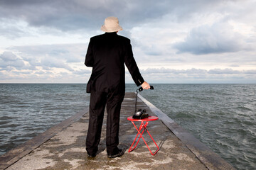 An unidentified businessman wearing a black suit on a dock answering an old black rotary telephone