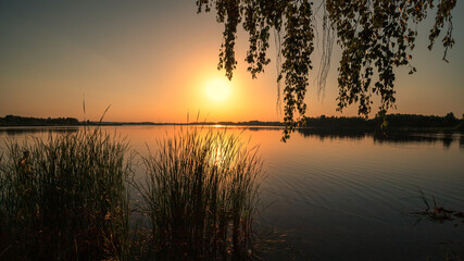 Scenic view of beautiful sunset or sunrise above the pond or lake at spring or early summer evening...