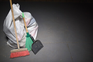 Broom and dust pan and trash bags garbage on the dirty dusty floor. Cleaning concept.