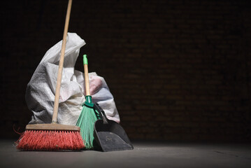 Broom and dust pan and trash bags garbage on the dirty dusty floor. Cleaning concept.