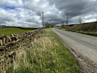 Black Hill Lane extends into the horizon beneath a striking sky, bordered by dry stone walls and fields on both sides, located in Steeton, Yorkshire, UK.