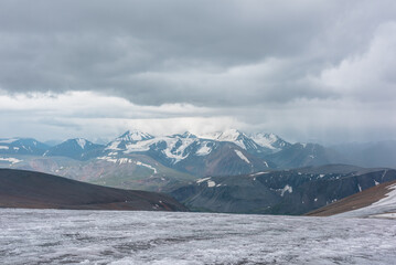 Dramatic panoramic view from big glacier to wide alpine valley and large snow-capped mountain range in rainy low clouds. Awesome vast landscape with high snowy mountains in rain under gray cloudy sky. - 788504326