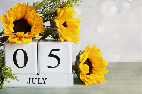 Workaholics Day. White wood calendar blocks with the date July 5th and beautiful sunflower bouquet with bokeh. Selective focus with blurred background. 