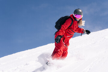 Woman snowboarder riding on slope of powdery snow in high mountains. Freeride at ski resort, amazing mountain peaks view