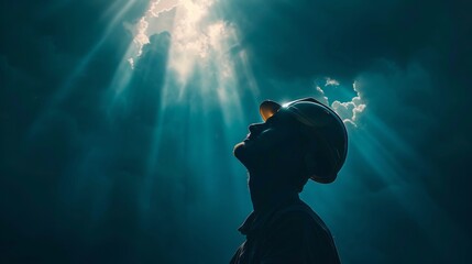 Construction worker in a hard hat, spotlighted by a strong overhead light, against a dark, moody sky - obrazy, fototapety, plakaty