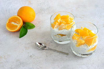 two glasses of dessert with chia seeds, yogurt and oranges and a spoon