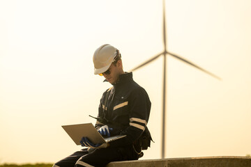 A technician in safety gear meticulously records data with a wind turbine in the backdrop at dusk.