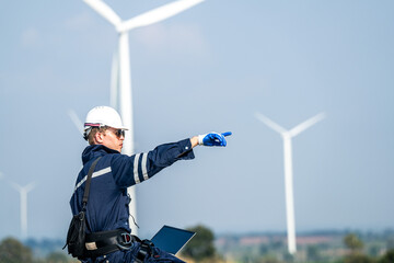 Focused engineer with a laptop conducts field analysis at a wind farm, wind turbines towering in...