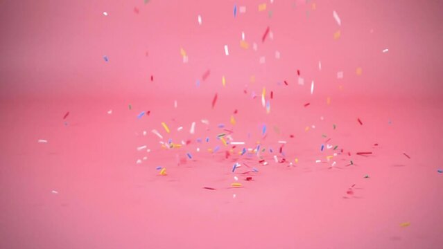 colorful sprinkles falling on pink background, decoration for cake and bakery, slow motion