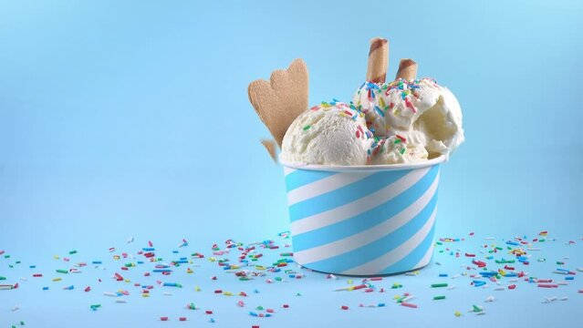 scoops of ice cream in bowl with strewed sprinkles, cigars and cookies on blue background, summer creative concept, copy space