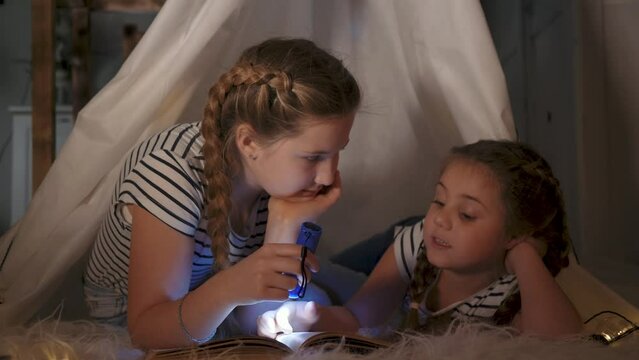 Happy family concept. kids with a flashlight in a tent. children read a book. kids shine a flashlight together at night. children read book before bed. kids shine flashlight into book. happy children