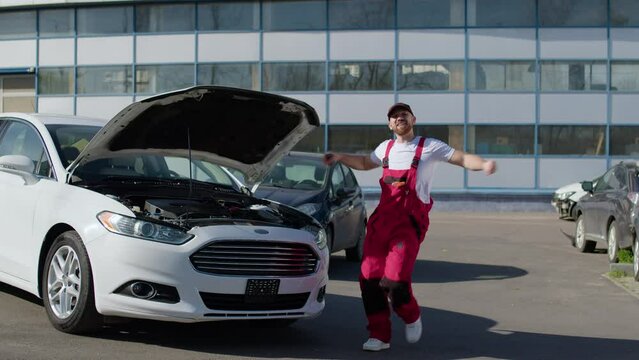 Mechanic joyfully dances beside repaired car celebrating successful restoration of vehicle and showcasing satisfaction of job well done in automotive service industry. Mechanic joyfully dances.