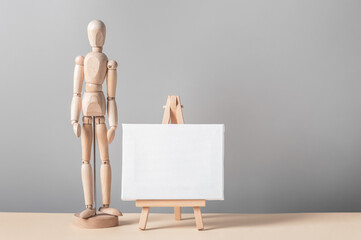 Creative composition with a miniature canvas on an easel and a wooden figurine of a man. Artistic...
