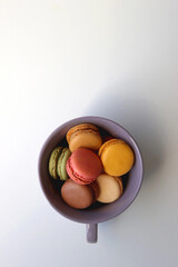 Purple cup filled with pastel macarons on white background. Top view. - obrazy, fototapety, plakaty