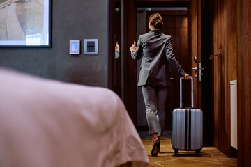 Rear view of businesswoman with suitcase leaving hotel room.