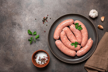 Fresh raw homemade sausages in a plate on a dark background. Top view, flat lay.