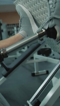Vertical shot of of athlete with prosthetic leg exercising on leg press machine in modern gym or fitness center. Fit man with physical disability does strength training using professional sports
