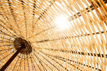 A close-up shot of a woven straw beach umbrella, showcasing texture and pattern with the sun shining through, taken from below.