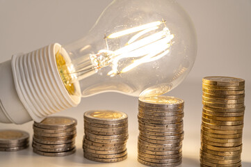 Light bulb lit, above stacks of coins. Increase in electricity tariffs, energy dependence, energy...
