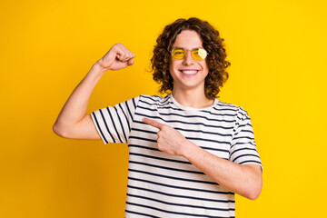 Photo portrait of handsome teenager guy show muscle point biceps wear trendy striped garment isolated on yellow color background