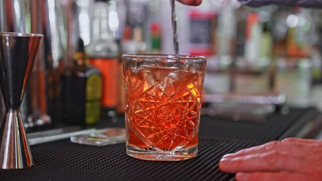Bartender with cocktail and orange peel preparing cocktail at the bar. Alcohol drinks, people and luxury concept