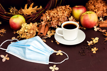 Cup of coffee, removed medical mask, blue surgical protective mask in autumn composition