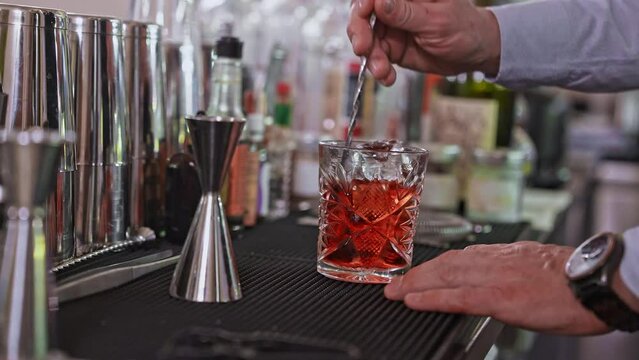 Bartender with cocktail and orange peel preparing cocktail at the bar. Alcohol drinks, people and luxury concept