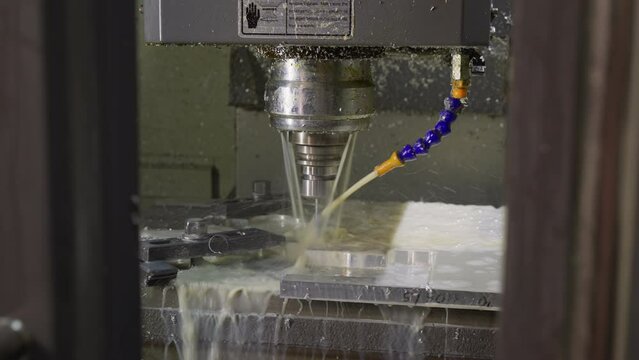 Coolant spray and metal shavings fly as CNC machine drills into metal at a workshop