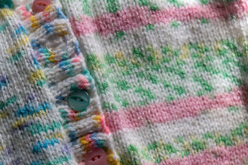 knitting background - hand knit baby cardigan in pink and green pastel colours with buttons 