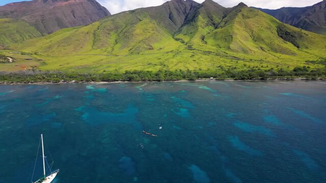 Kayakers and sailing boat explore coral reefs in the shallows of Maui coast, Hawaii. 